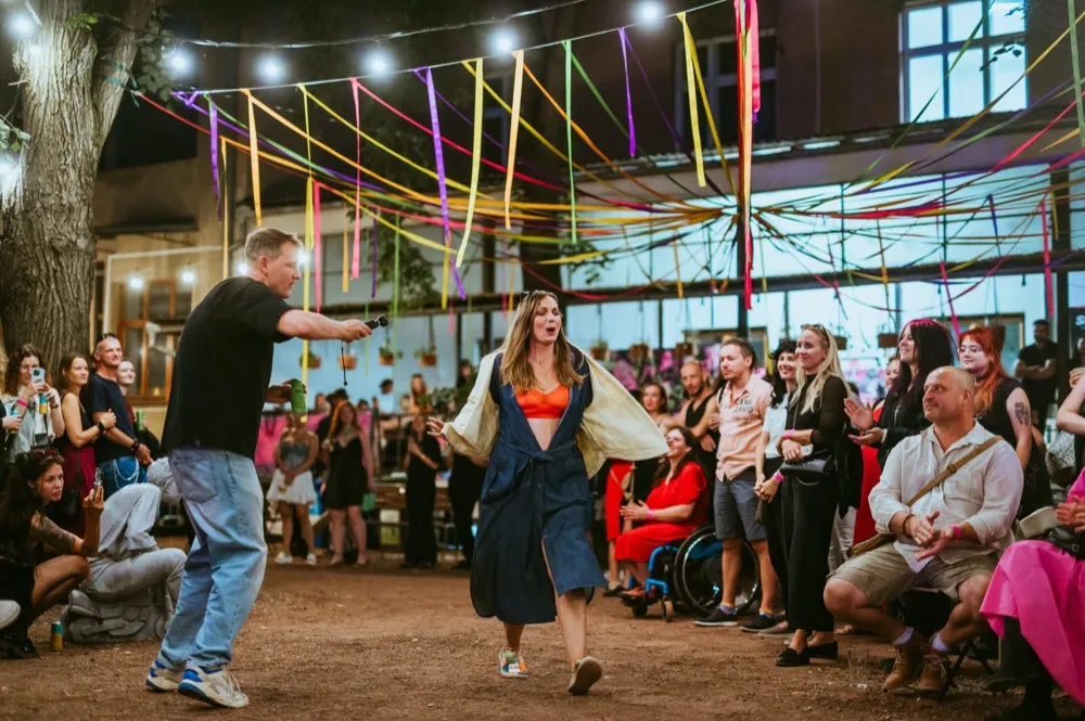 Modelka v džínovém kabátě prochází mezi diváky pod barevnými fáborky