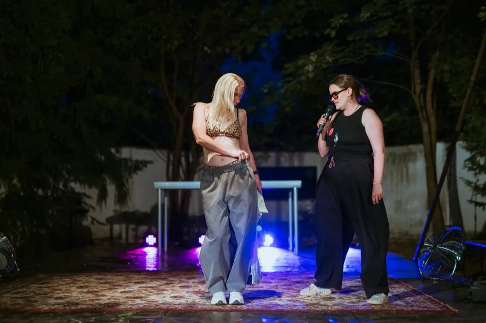 Moderátorka s mikrofonem uvádí modelku na koberci uprostřed parku